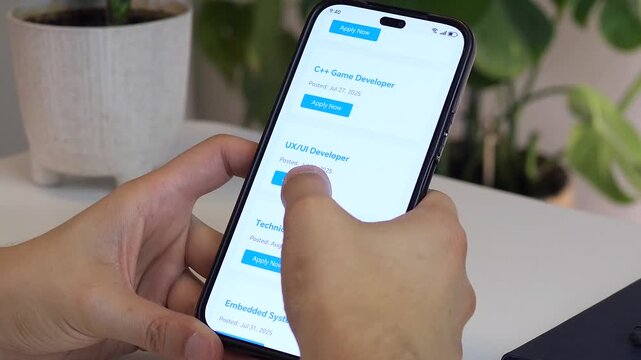 Close-up footage of a man's hands navigating a job search website on his smartphone, carefully scrolling through IT developer positions before selecting and applying for the perfect role. 