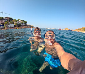 Father and son wearing snorkeling masks and taking a selfie in the clear waters of the mediterranean sea