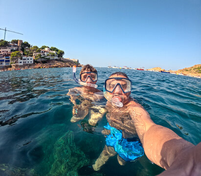 Father and son wearing snorkeling masks and taking a selfie in the clear waters of the mediterranean sea