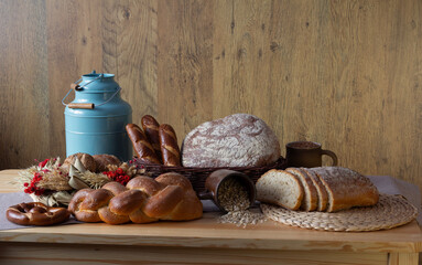 Traditional bakery products no. 7 in an organized composition. Bread, loaves, rolls, croissants, pretzels, challah, ears of grain, baked goods, a blue metal watering can, traditional table decoration