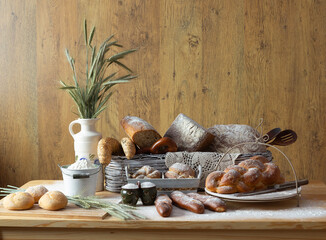 Traditional bakery products number 3 in an organized composition. Bread, loaves, rolls, croissants, pretzels, challah, ears of grain, baked goods, porcelain jug, wooden spoons, traditional decoration
