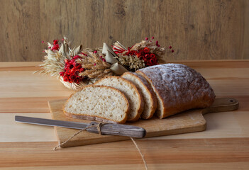 freshly sliced bread on a wooden cutting board no. 2, bread cutting knife, delicious breakfast for morning coffee, decorative bouquet of grains, kitchen knife for slicing bread