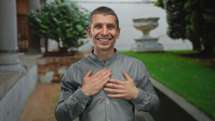 Fototapeta premium Man smiling outdoors with hands on chest in a peaceful green park setting showing happiness and contentment during a day out.