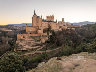 Aerial view of the AlcÃ¡zar de Segovia, a medieval castle with its imposing stone architecture silhouetted against the soft glow of the evening sky, Segovia, Castilla y LeÃ³n, Spain.