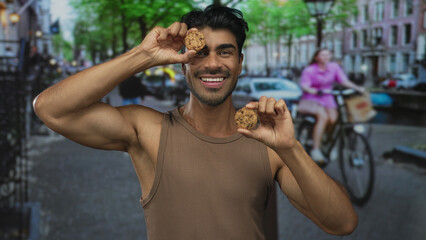 Man smiles and holds two chocolate cookies with raised arms on urban street; joyful delight...