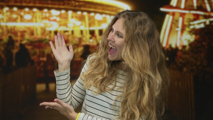 Woman holds her hands presenting a carnival full of lights as a blonde young host smiling with amusement at the night attraction.