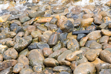 Smooth wet river stones with water flowing over them, creating a natural textured surface in shades of brown, gray, and black.