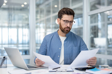 Dedicated professional thoroughly analyzing documents at a contemporary desk within a bright office setting. The environment includes modern tools, a laptop, and organized workspace