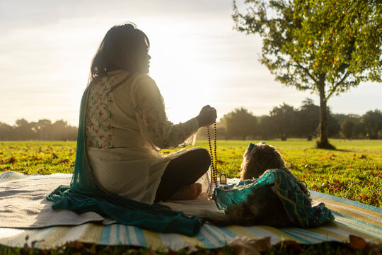 Indian woman meditating outdoors with prayer beads and dog