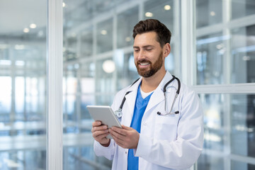 A healthcare professional wearing a white coat and stethoscope smiles, using a digital tablet in a contemporary medical environment, showcasing technology integration in modern medicine.