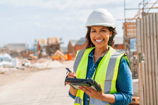 Young woman builder construction manager uses rugged tablet to record data on construction site - Powered by Adobe