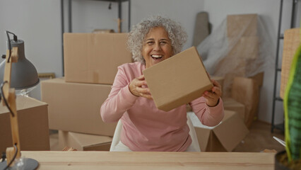 Woman happily unpacking boxes in a new home surrounded by cardboard in a cozy living room setting,...