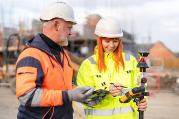 Construction engineers surveyors collaborating on site, using modern theodolite for surveying and measurement, and sharing expertise in safety gear