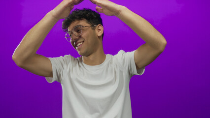 Man smiling broadly raises arms to form roof gesture in purple studio; joy celebration optimism...