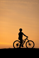 Obraz premium ニュージーランド ホキティカ・ビーチ 夕陽に照らされた自転車に乗った子供のシルエット