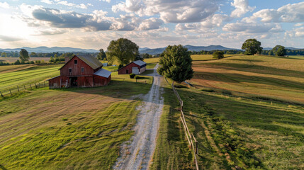 Picturesque countryside farmhouse with large red barn and gravel driveway, surrounded by lush green fields and distant mountains under bright sky. scene evokes sense of tranquility and rural charm