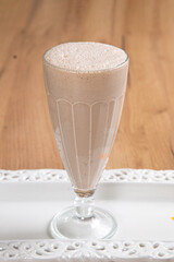 Creamy chocolate cocktail in a tall glass goblet on a light wooden table