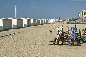 Row of white beach huts and four-wheeled tricycles for children riding on the seawall at De Panne,...