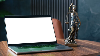 Laptop with blank screen positioned on wooden table beside a bronze Lady Justice statue, symbolizing law and order in a modern office environment with a professional atmosphere