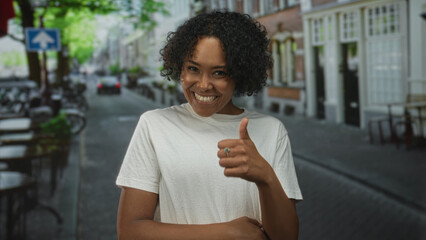 Woman smiling and pointing her index finger on narrow cobblestone street beneath brick building facade; joy.