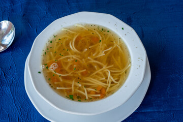 Traditional Polish noodle soup (rosół) with carrots and herbs in white bowl
