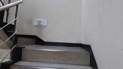 POV walking up an indoor stairwell with a stainless handrail; quiet landing and emergency exit sign inside a simple apartment/office building.