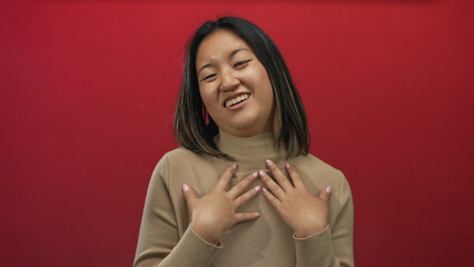Young woman smiling with hands on chest against a vibrant red background expressing happiness and...
