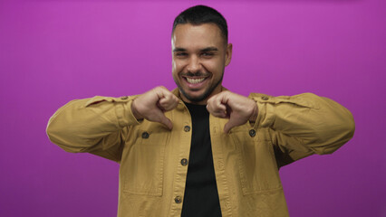 Frontal view of man wearing yellow shirt smiling while showing double thumbs down gesture in studio setting; playful.