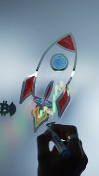 Hand rocket ship emoji on foggy window pane with crypto chart visible on monitor inside