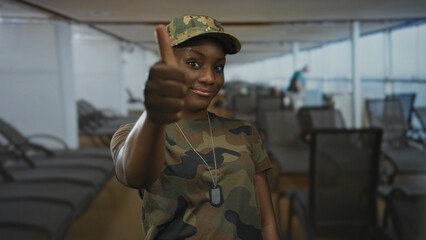 Young african american woman in camouflage military uniform shows thumbs up and thumbs down on boat...