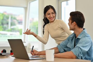 A professional team having a friendly conversation while working on a laptop in an office, showing collaboration and teamwork