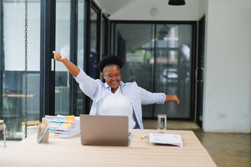 Young african american businesswoman stretching with arms raised celebrating success while working...