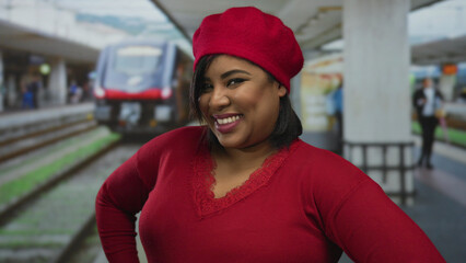 Woman smiling confidently at train station wearing red beret and sweater standing near railway platform outdoor.
