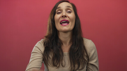 Fototapeta premium Hispanic young woman cups hand to mouth shouting against red wall; urgent alert announcement expression.