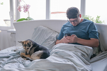 Man looking at screen mobile phone smartphone sitting in the bed in the morning and eating cereal