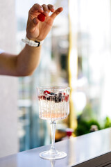 Bartender garnishing cocktail with fresh blackberry, Close-up of bartender placing a fresh blackberry into a chilled cocktail glass with ice and berries, highlighting mixology and drink presentation.
