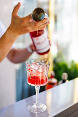 Bartender pouring red cocktail over ice in glass, Close-up of bartender pouring bright red cocktail into a glass with ice cubes, showcasing mixology, refreshing drinks, and bar service.