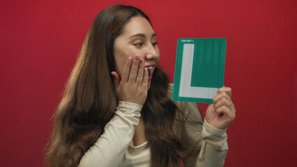Young hispanic woman holds a green l plate and smiles in studio setting; confidence progress practice achievement.