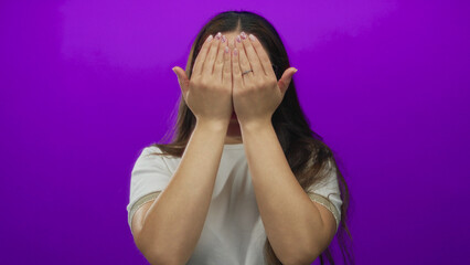 Young hispanic woman wearing glasses raises palms and covers mouth in purple studio; celebration...