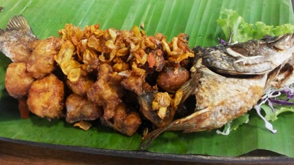 Crispy deep-fried fish with garlic topping served on banana leaf with spicy Thai fish sauce, authentic Thai seafood dish