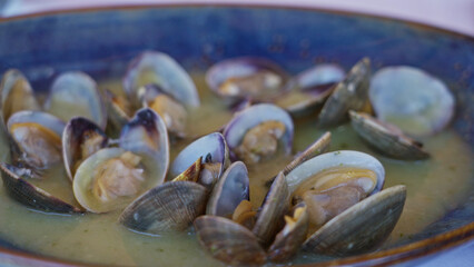Clams in a blue bowl indoors at a mediterranean restaurant showcasing fresh seafood with sauce served on a table with a silver spoon highlighting the culinary elegance and simplicity