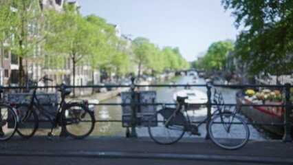 Blurred view of bicycles on a bridge over amsterdam canals with trees in the background, creating a...