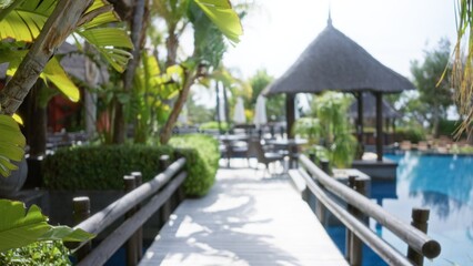 Blurred tropical resort pathway with bokeh effect, framed by lush green palms and thatched structures reflecting luxury and serenity.