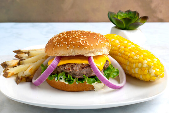 cheese burger with  fries and corn  on the cob