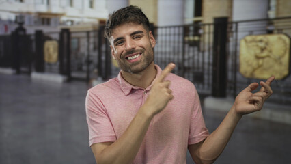 Smiling young man wearing pink shirt pointing finger to iron gate on urban street; optimism hope...