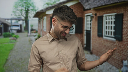 Young man casually uses hand to play air guitar gesture at building entrance on a sunny morning; imagination playfulness fun joy.