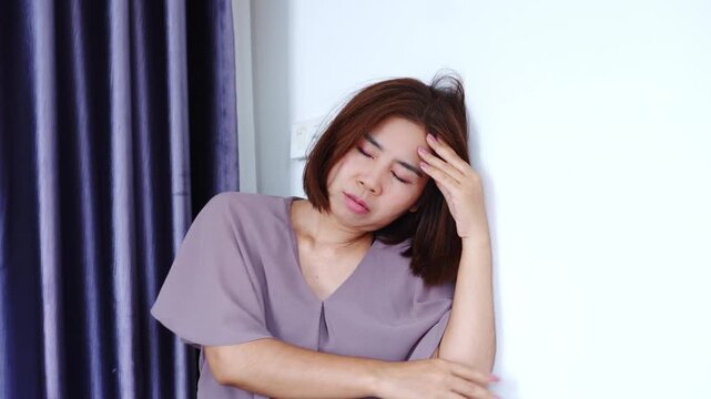 Asian woman suffering from dizziness, vertigo and loss of balance, holding head and leaning against the wall due to Meniere's disease, inner ear problems, or postural hypotension, symptoms of fainting