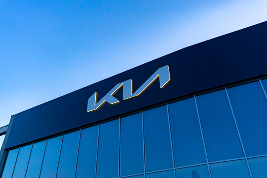 Illuminated Kia logo on glass facade of a car dealership in Kalisz, visible at dusk against the sky