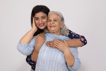 Naklejka premium Indian smiling young daughter and old mother hug embrace isolated on white studio background. Concept of Senior mother and daughter love bonding
