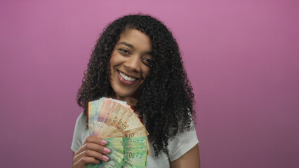 Woman smiles and holds south african rand banknotes against pink background in studio; wealth...